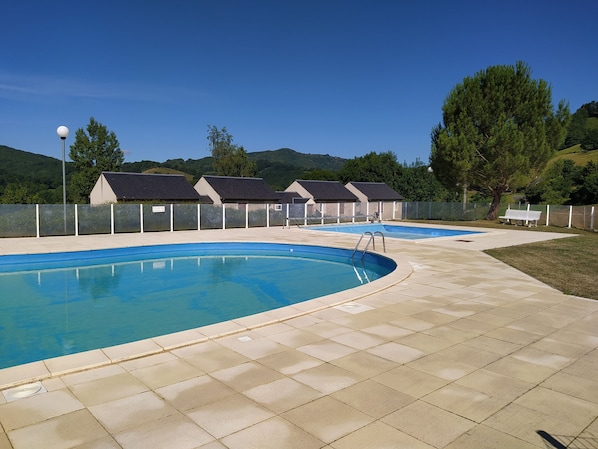 A swimming pool with a tiled deck, surrounded by a fence and trees.