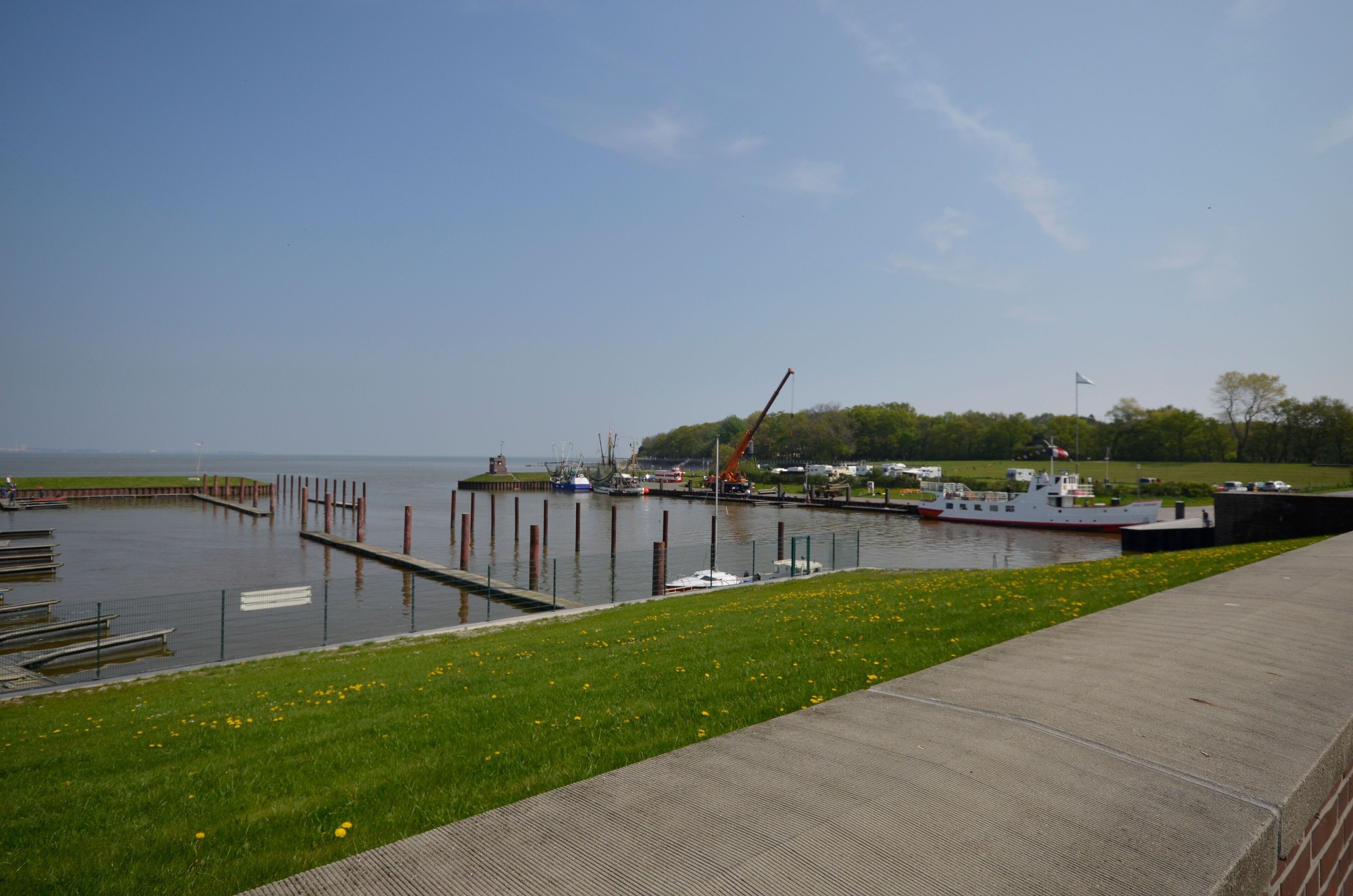 A marina with boats docked, a crane, and a grassy area with a pathway.
