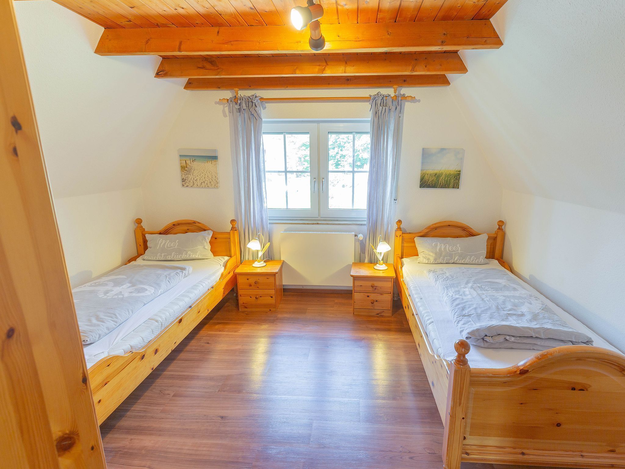 Ein Zimmer mit zwei Holzbetten, einem Fenster mit Vorhängen und einem Deckenventilator.