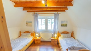 A room with two wooden beds, a window with curtains, and a ceiling fan. - Ferienhaus Newerenczuk, Vermietungsservice Dangast - Ferienhaus Newerenczuk (Varel)