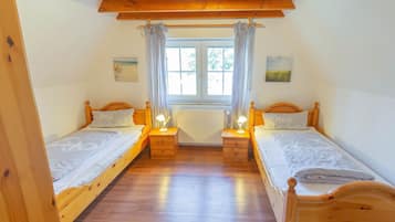 A room with two wooden beds, a window with curtains, and a ceiling fan.