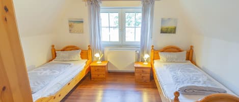 A room with two wooden beds, a window with curtains, and a ceiling fan.