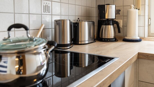 A modern kitchen with a black induction cooktop, stainless steel pots, a coffee maker, and a white candle on the counter. - Ferienhaus Newerenczuk, Vermietungsservice Dangast - Ferienhaus Newerenczuk (Varel)