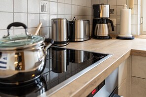Eine moderne Küche mit einem schwarzen Induktionskochfeld, Edelstahlkochgeschirr, einer Kaffeemaschine und einem weißen Teelicht auf der Arbeitsfläche.