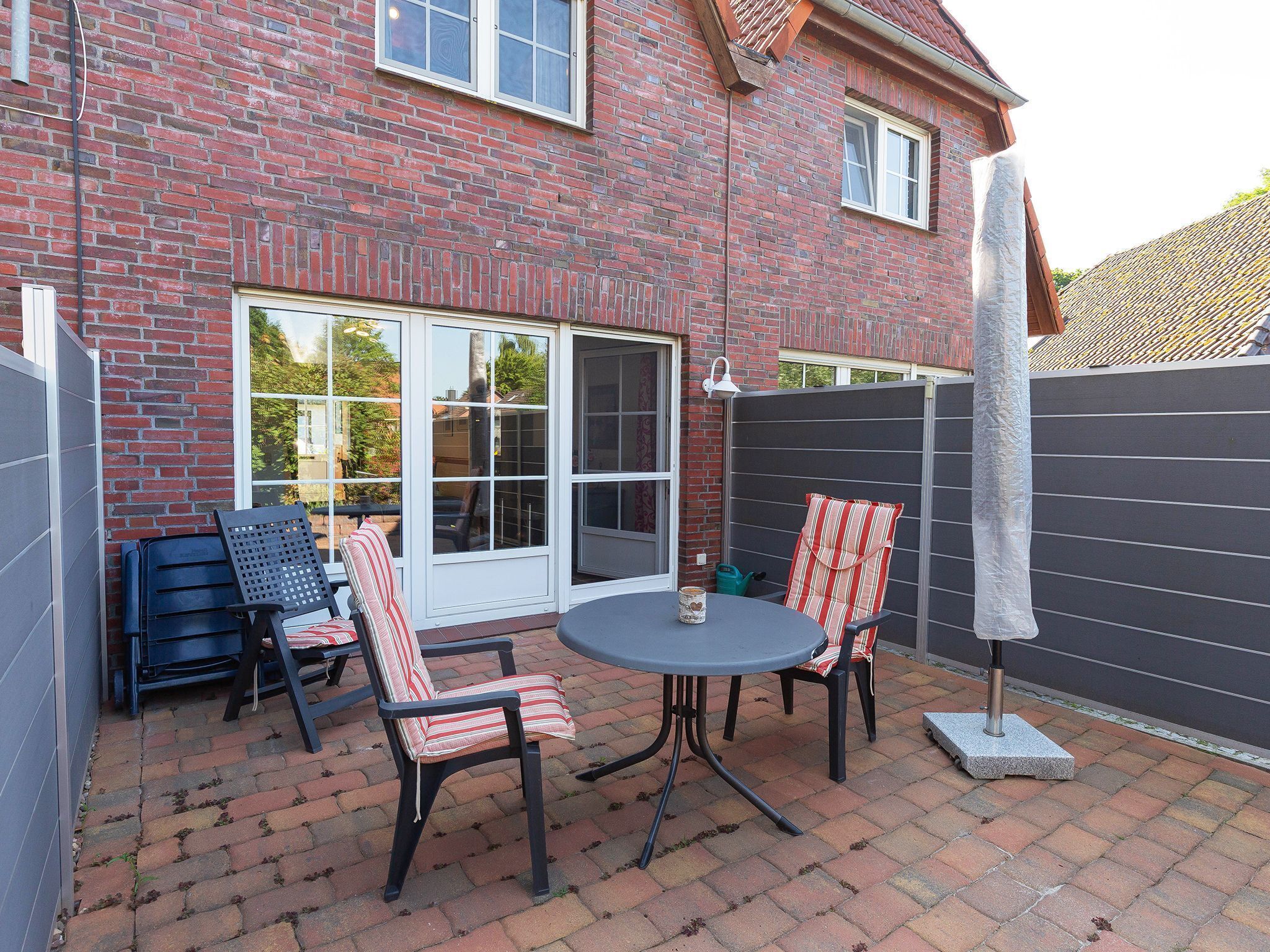 A patio with a brick wall, two chairs, a table, and a large umbrella.