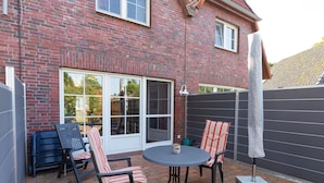 A patio with a brick wall, two chairs, a table, and a large umbrella. - Ferienhaus Newerenczuk, Vermietungsservice Dangast - Ferienhaus Newerenczuk (Varel)