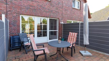 A patio with a brick wall, two chairs, a table, and a large umbrella.