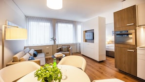 A modern hotel room with a dining area, a sofa set, a TV, and a kitchenette.