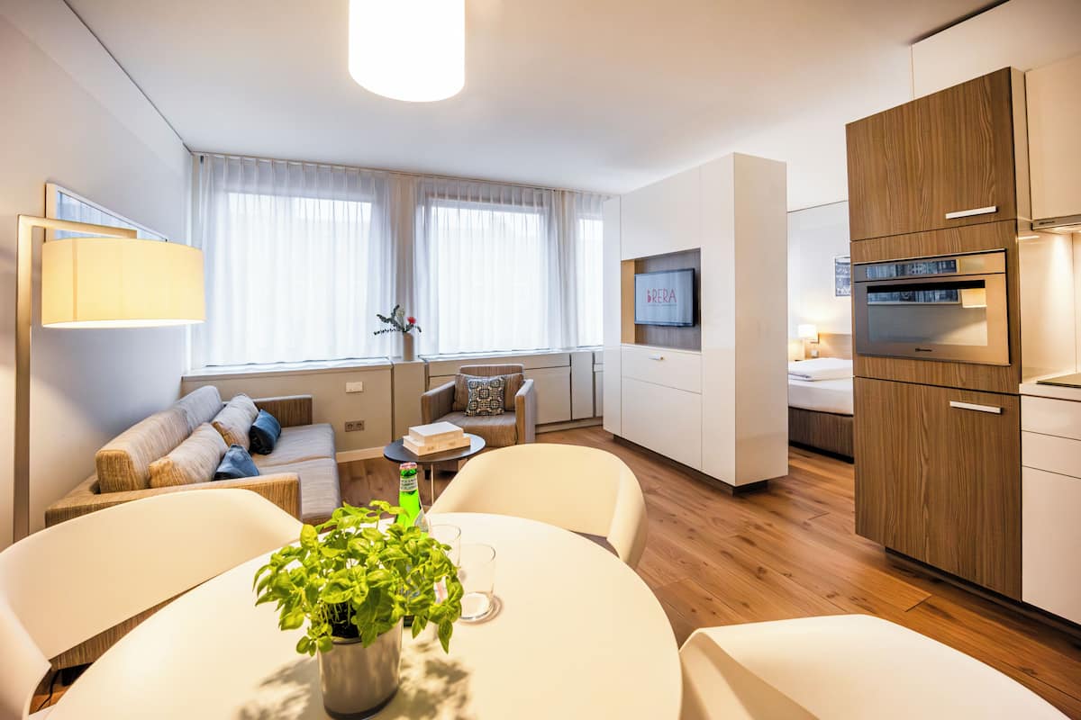 Ein modernes Hotelzimmer mit Essbereich, einer Sofaecke, einem Fernseher und einer Küchenzeile.