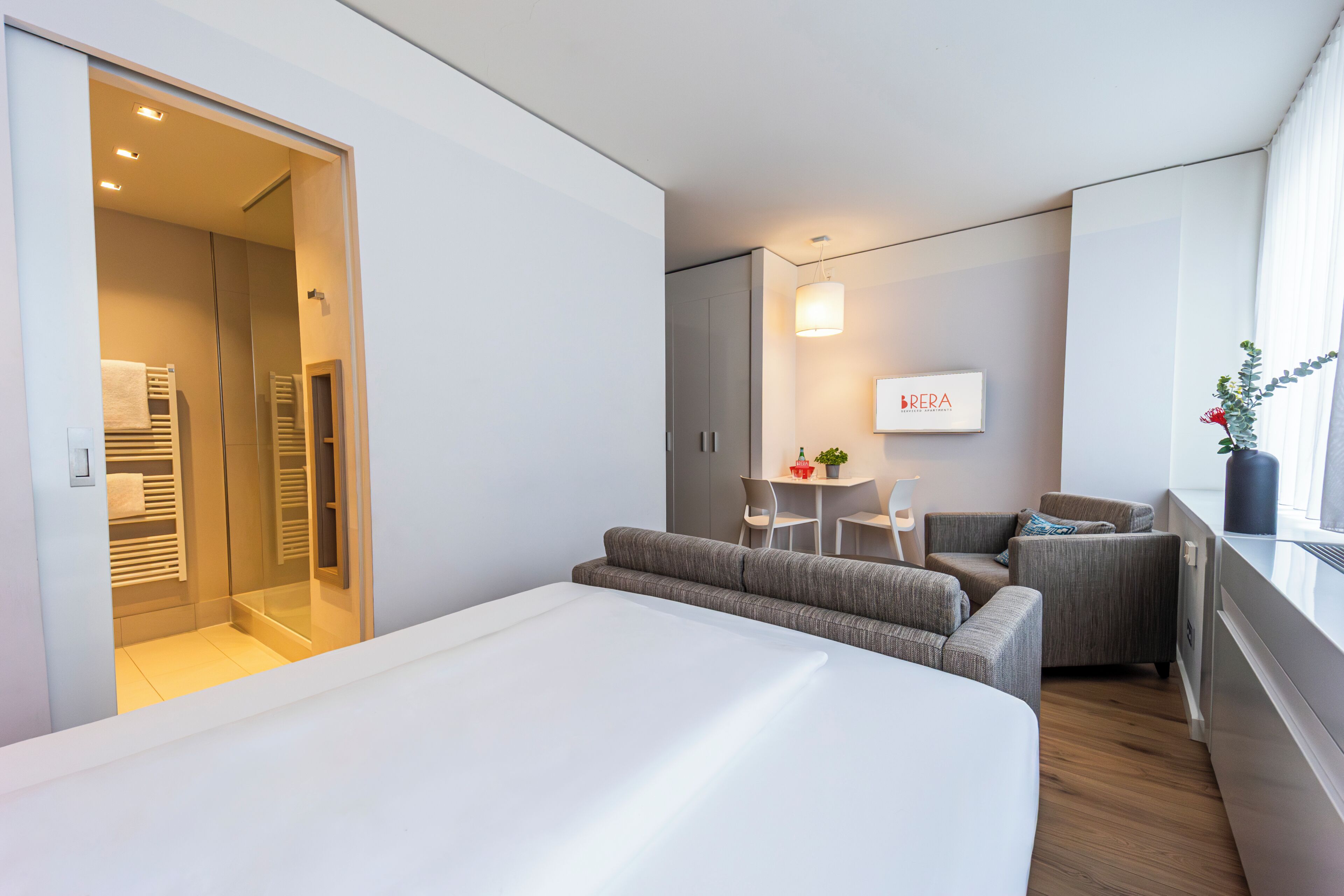 Une chambre d’hôtel moderne comprenant un lit, un coin salon avec une table et des chaises, un canapé et une grande fenêtre.