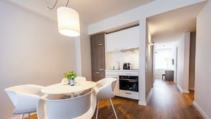 A modern kitchen with white cabinets, a built-in oven, and a dining area with a round table and white chairs.