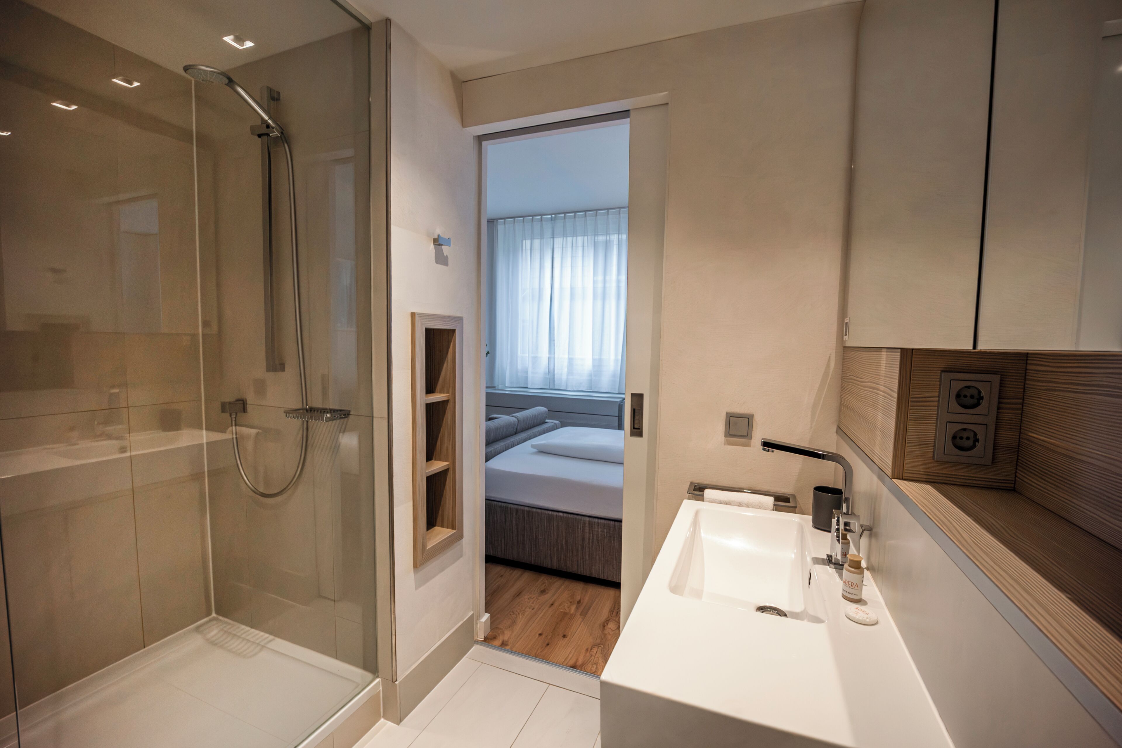 Ein modernes Badezimmer mit einer gläsernen Duschkabine, einem weißen Waschbecken und Holzboden.