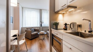 A modern kitchen with a sink, stove, and countertop. There is a dining area with a table and chairs, and a sofa.