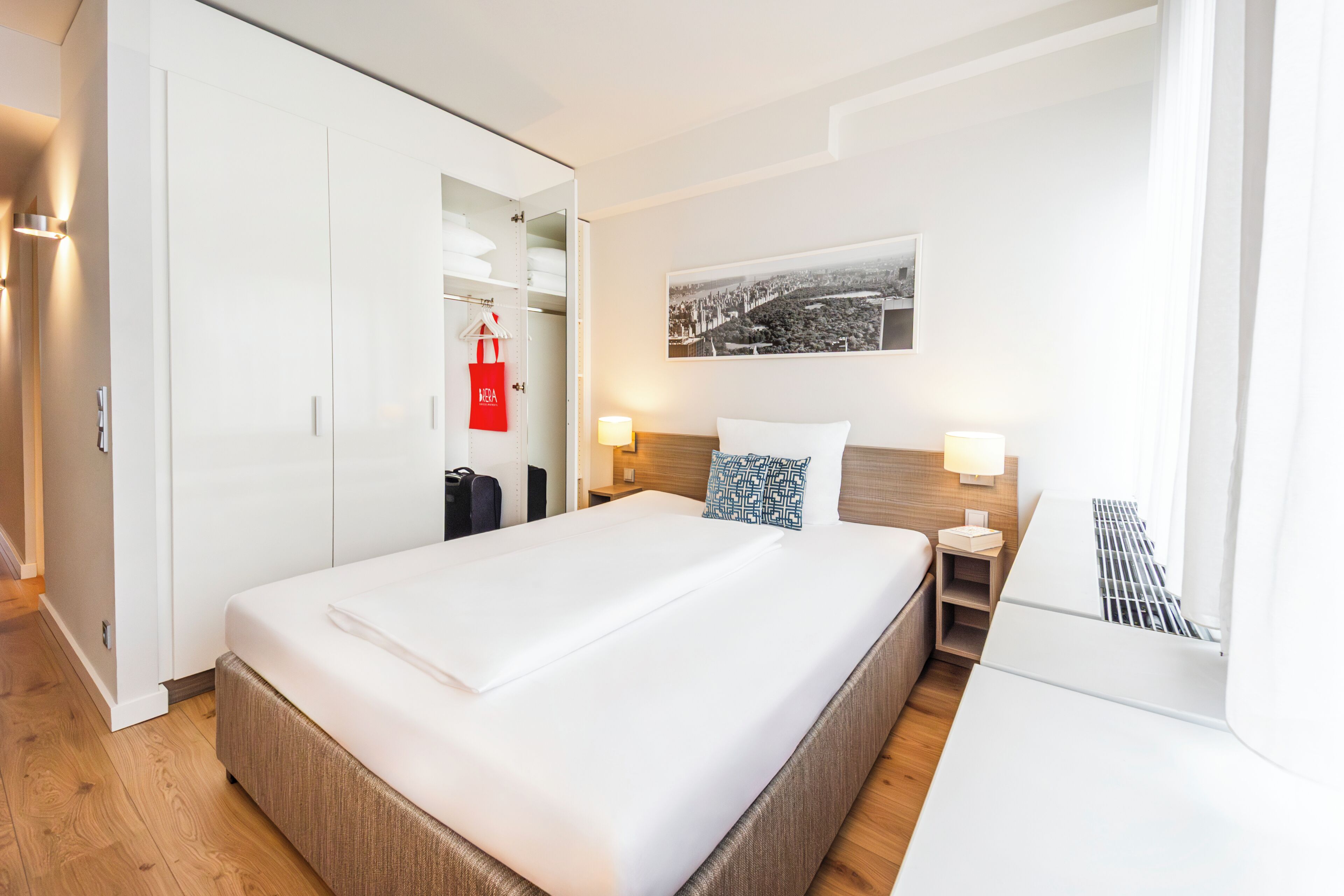 A hotel room with a large bed, a wardrobe, a bedside table with a lamp, and a wall-mounted picture.