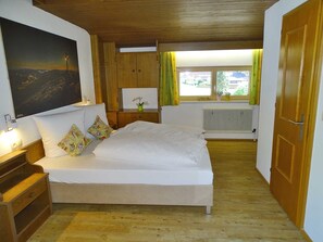 A bedroom with a bed, wooden wardrobe, a radiator, a window with curtains, and a painting on the wall.