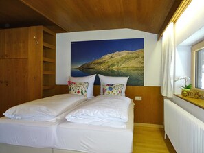 A bedroom with a bed, wooden wardrobe, a large landscape painting, and a window with curtains.