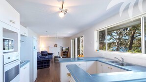 A modern kitchen with a large window, a dining area with a TV, and a cozy seating area. - Lakeside Retreat @ Smiths Lake (Smiths Lake)