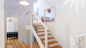 A staircase with wooden steps and white railings leading to a bedroom with a bed and a chair. - Lakeside Retreat @ Smiths Lake (Smiths Lake)