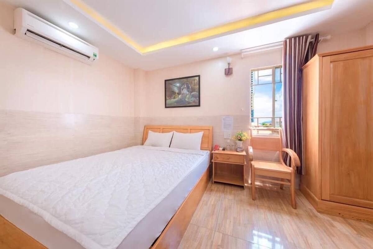 A hotel room with a bed, desk, chair, wardrobe, and an air conditioning unit.