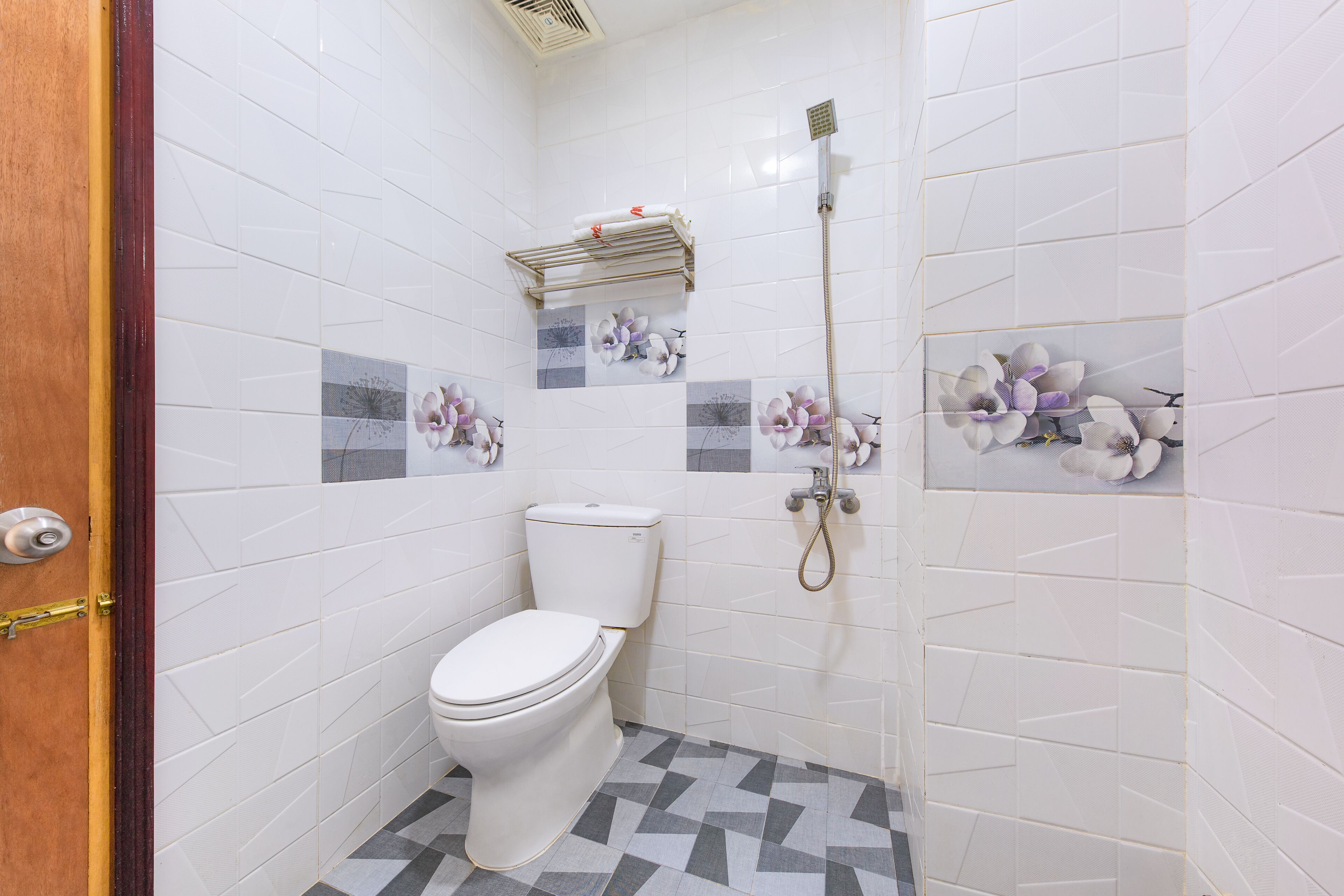 Un baño con azulejos blancos, un inodoro, una ducha y un perchero para toallas.