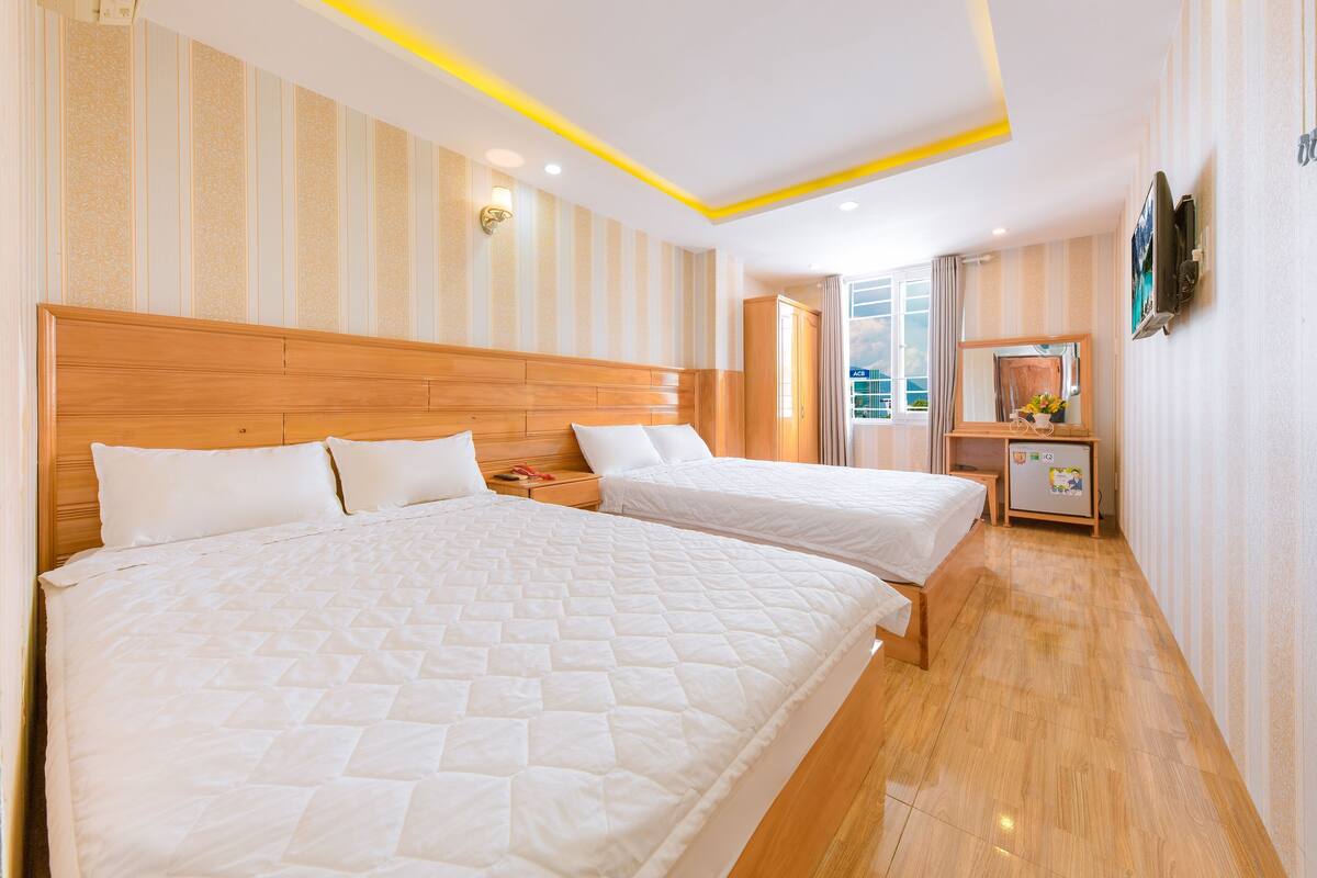 A hotel room with two beds, a wooden headboard, a nightstand, a TV, and a window with curtains.
