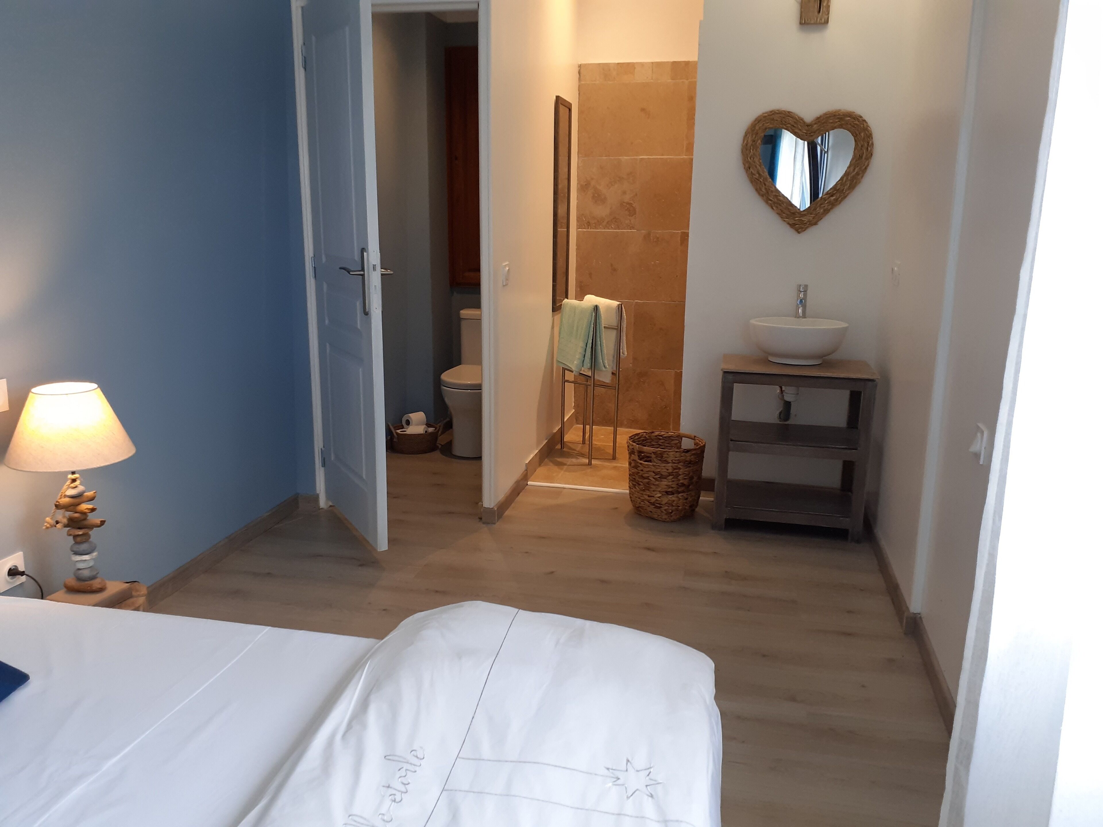 Een hotelkamer met een bed, een bedlamp, een badkamer met toilet, een wastafel en een spiegel in de vorm van een hart.