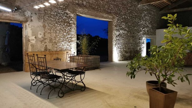 An outdoor dining area with a stone wall backdrop, a wooden table, and chairs. - Dominique and Eric welcome you to their large, characterful Mas with heated swimming pool. (Verquiéres)