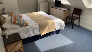Un dormitorio con cama, escritorio, silla, radiador y tragaluz.