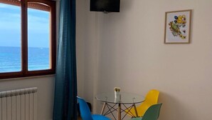 A room with a wooden floor, a window with curtains, a table with chairs, a television on the wall, and a framed picture. - Mondello Beach Rooms (Palermo)