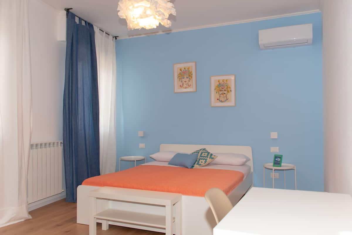 A bedroom with a bed, a bedside table, a chair, a radiator, and a wall-mounted air conditioner.