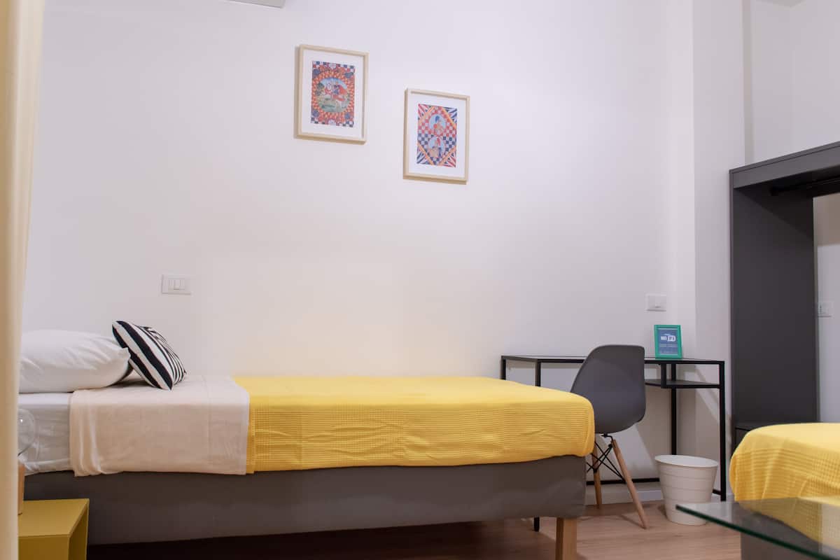 A small, modern room with a bed, a desk, and two framed artworks on the wall.