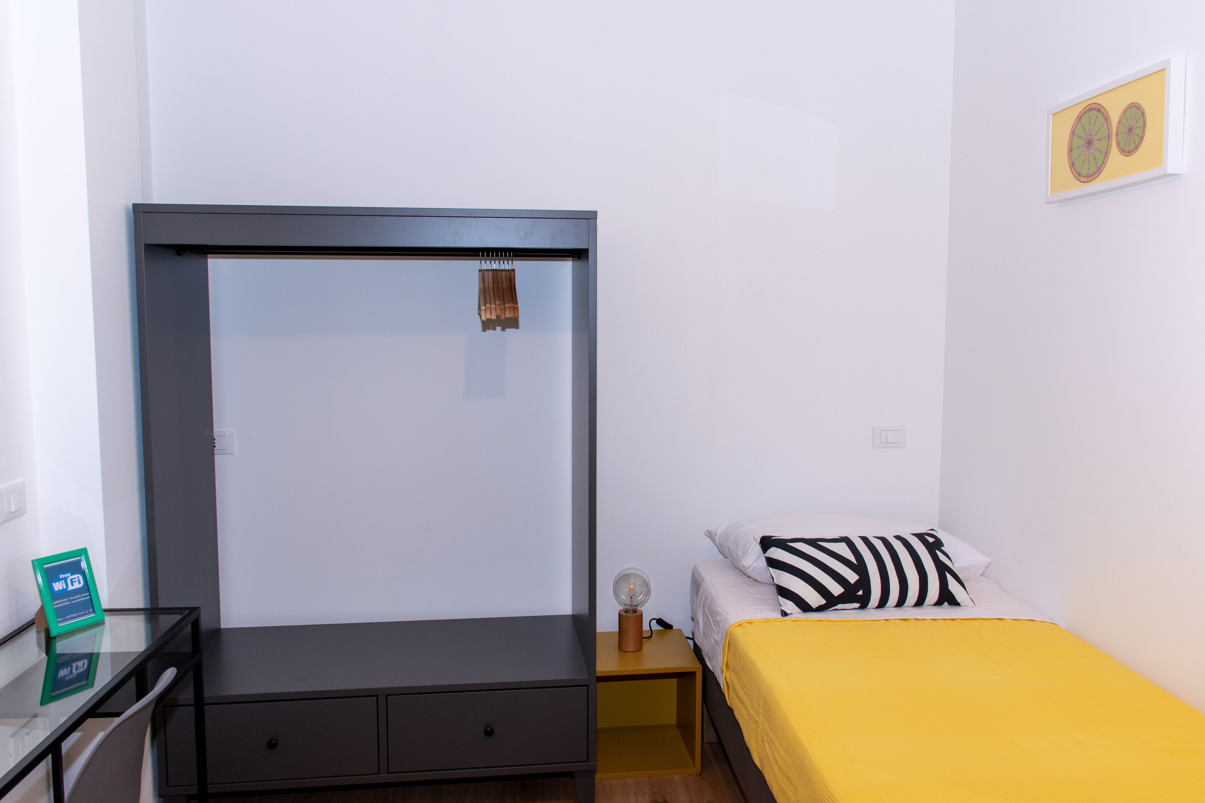 Un dormitorio con cama, mesita de noche, armario y una pequeña mesa con lámpara.