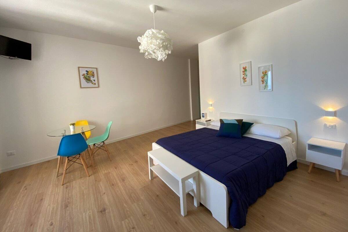A modern bedroom with a large bed, bedside tables, a bench, and a dining area with chairs.