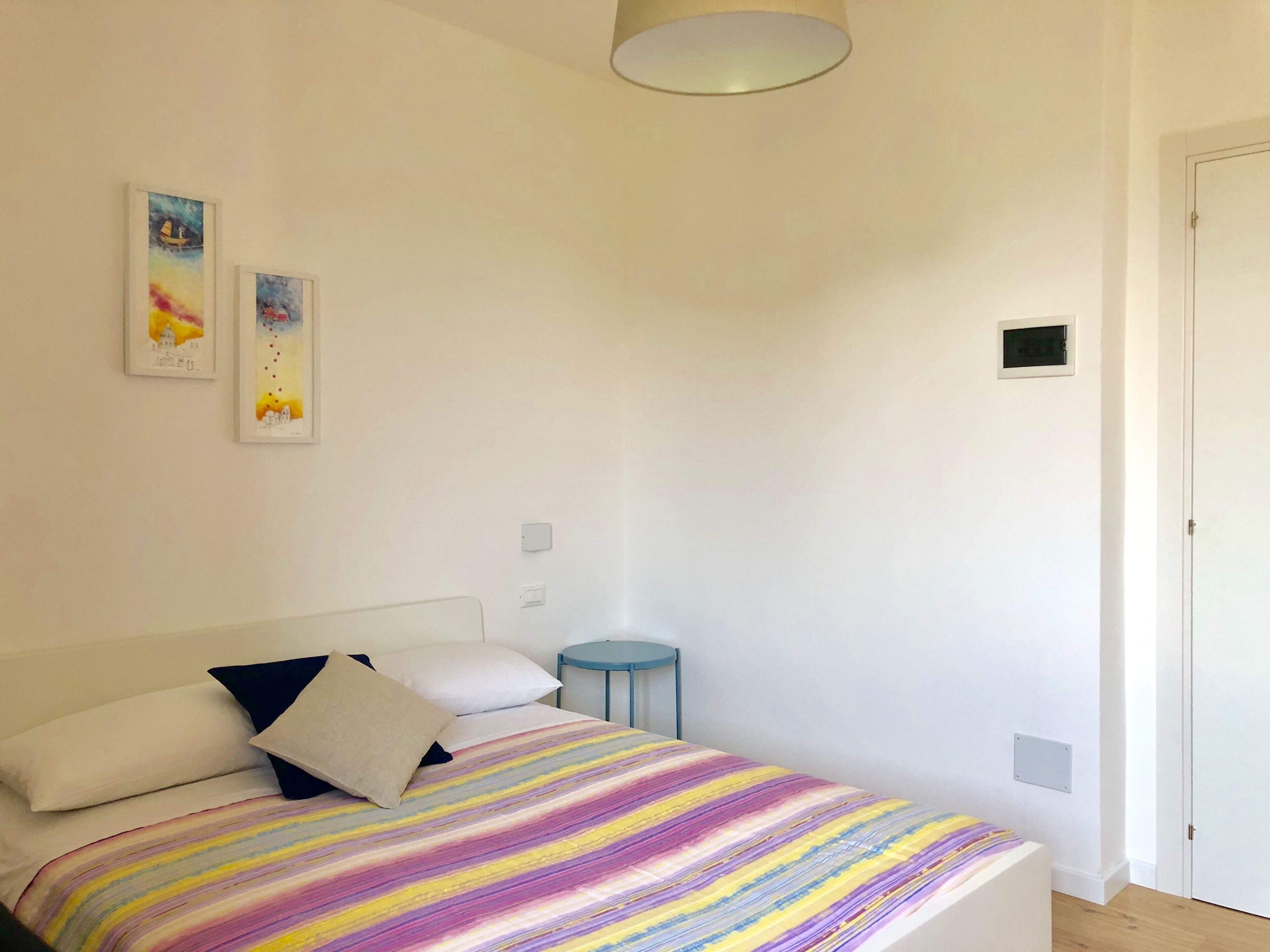 A bedroom with a bed, pillows, a bedside table, and two wall-mounted artworks.