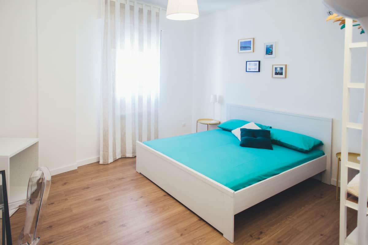 A bedroom with a bed, a nightstand, a lamp, and a window with curtains.