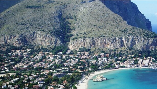 A coastal town with a mountain backdrop, a beach, and a boat docked near the shore. - Mondello Beach Rooms (Palermo)