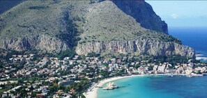A coastal town with a mountain backdrop, a beach, and a boat docked near the shore. - Mondello Beach Rooms (Palermo)