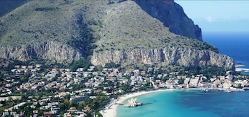 Uma vila costeira com montanhas ao fundo, uma praia e um barco ancorado perto da costa.