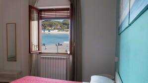 A bedroom with a bed, a window with a view of a beach, and a radiator. - Mondello Beach Rooms (Palermo)