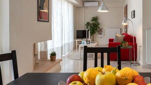 A modern living room with a dining area, featuring a table with fruits, a sofa, and a TV. - Magnificent 76m² homm Penthouse 6th, Acropolis View (Athens)