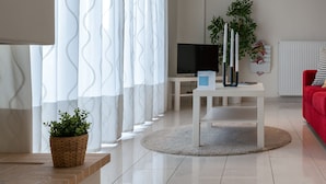 A modern living room with a flat-screen TV, a white coffee table, a red sofa, and a large window with white curtains. - Magnificent 76m² homm Penthouse 6th, Acropolis View (Athens)