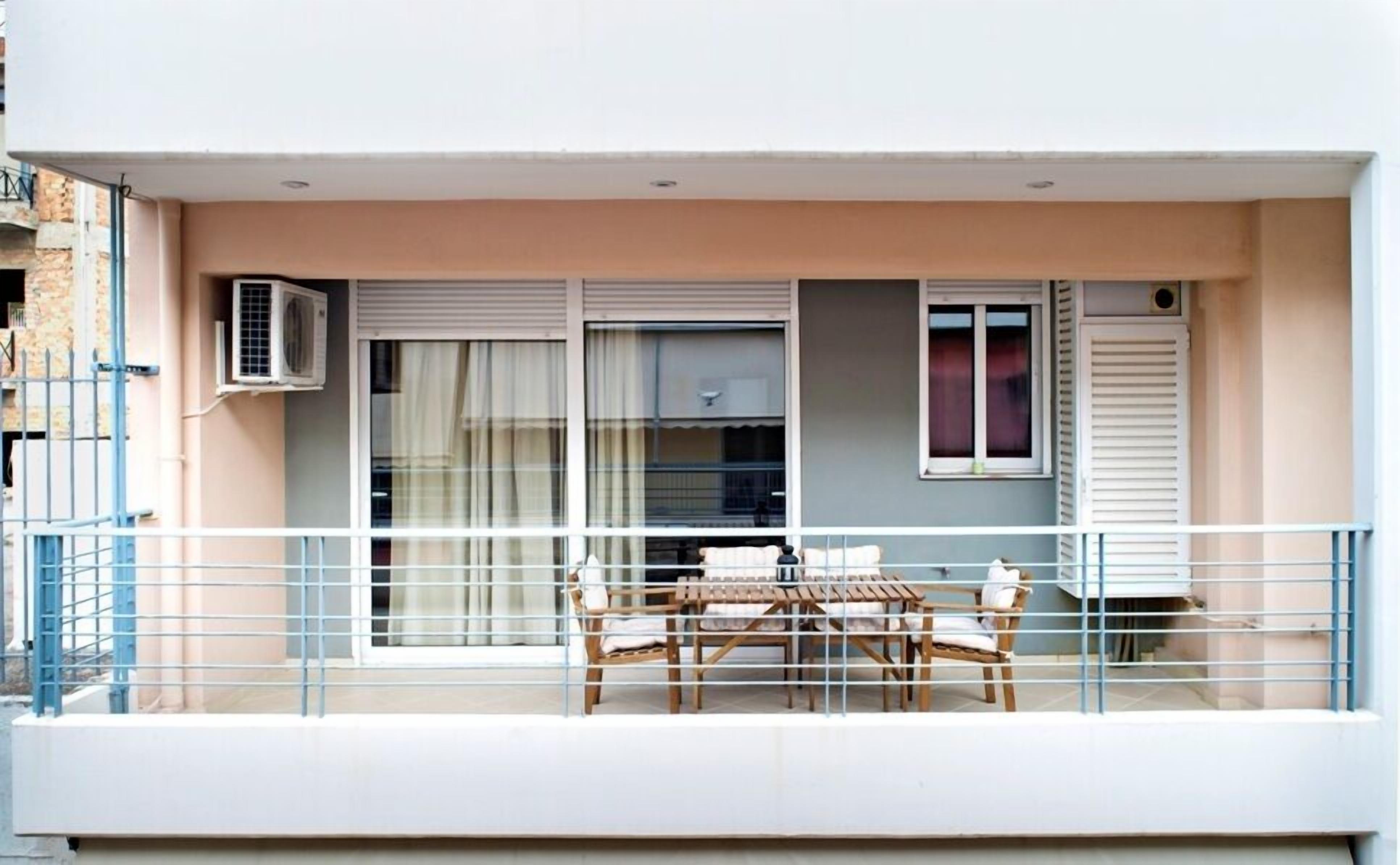A balcony with a table and chairs, air conditioning unit, and windows with shutters.