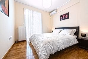 Ein Schlafzimmer mit Bett, Heizkörper, einem Fenster mit Vorhängen, einer Wand-Klimaanlage und einem Nachttisch mit Lampe.