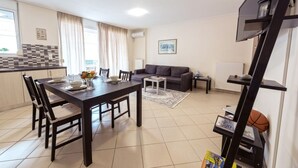 A modern living room with a dining area, a grey sofa, and a TV mounted on the wall. - Magnificent 101m² homm Apartment, 4th (Athens)