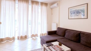 A living room with a brown sofa, a coffee table with books, and a large window with sheer curtains. - Magnificent 101m² homm Apartment, 4th (Athens)