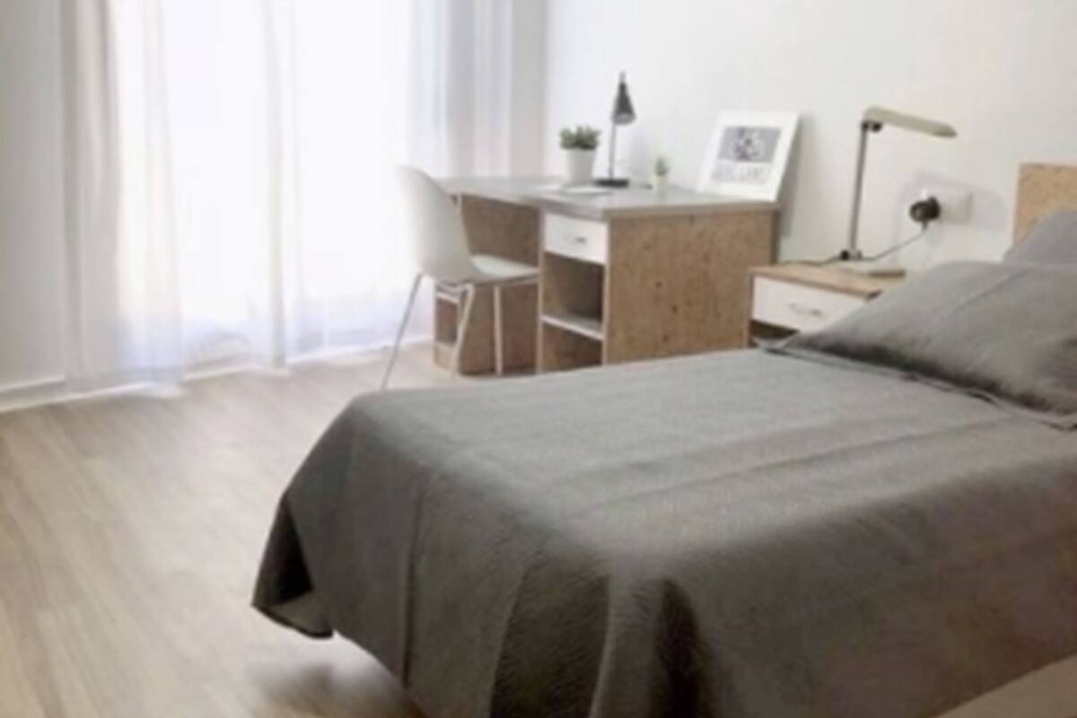 A bedroom with a bed, a desk, a chair, and a nightstand.