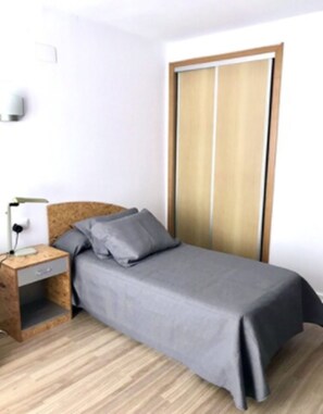 Un dormitorio con cama, mesita de noche, cabecera de madera, luz empotrada en la pared y puerta corrediza.