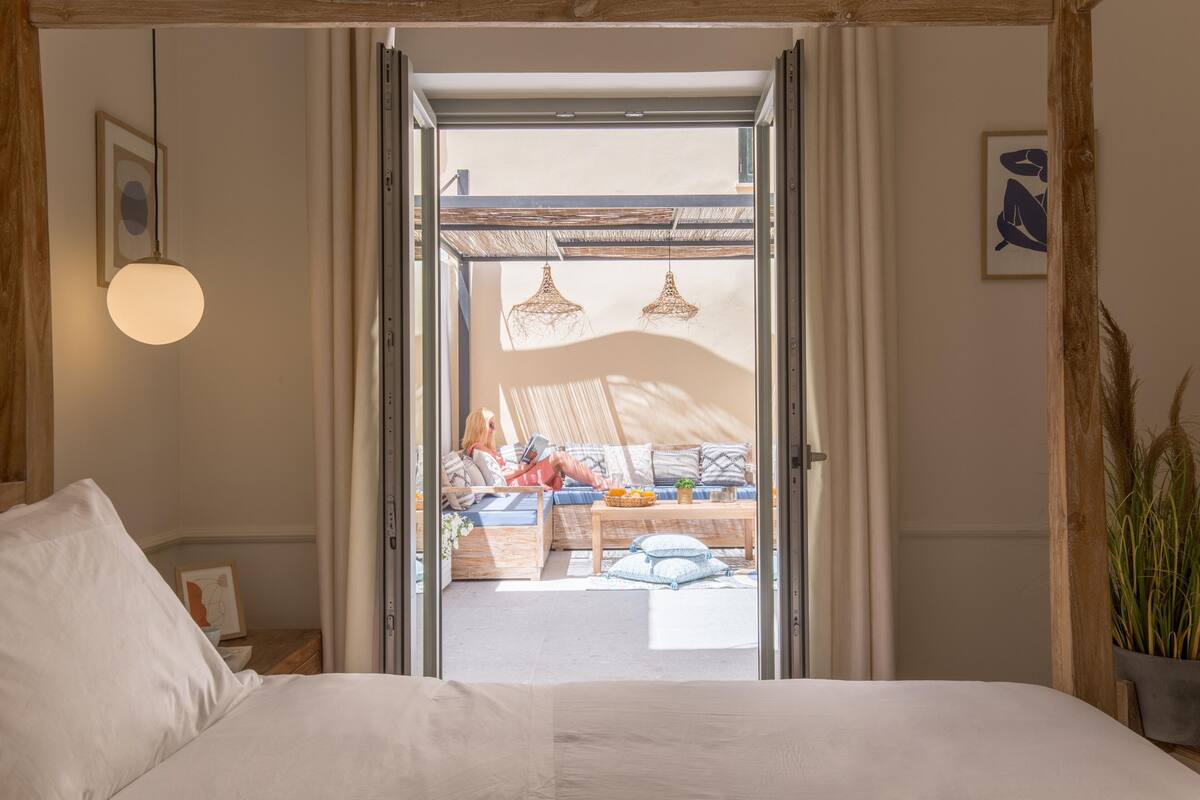 Quarto com cama, teto de madeira, janela e vista para uma área de estar externa.