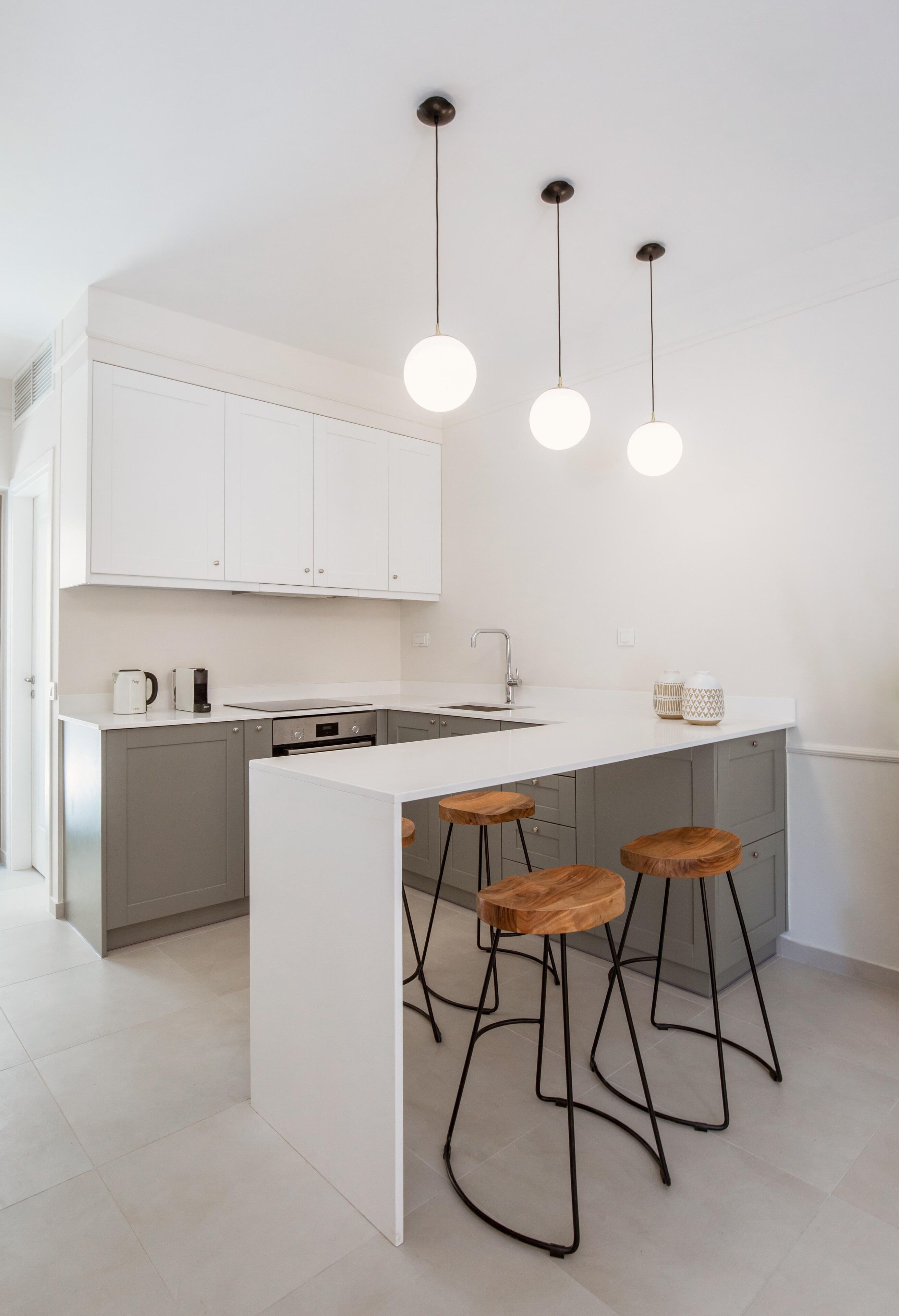 Una cocina moderna con armarios blancos, una isla central con taburetes e iluminación colgante.