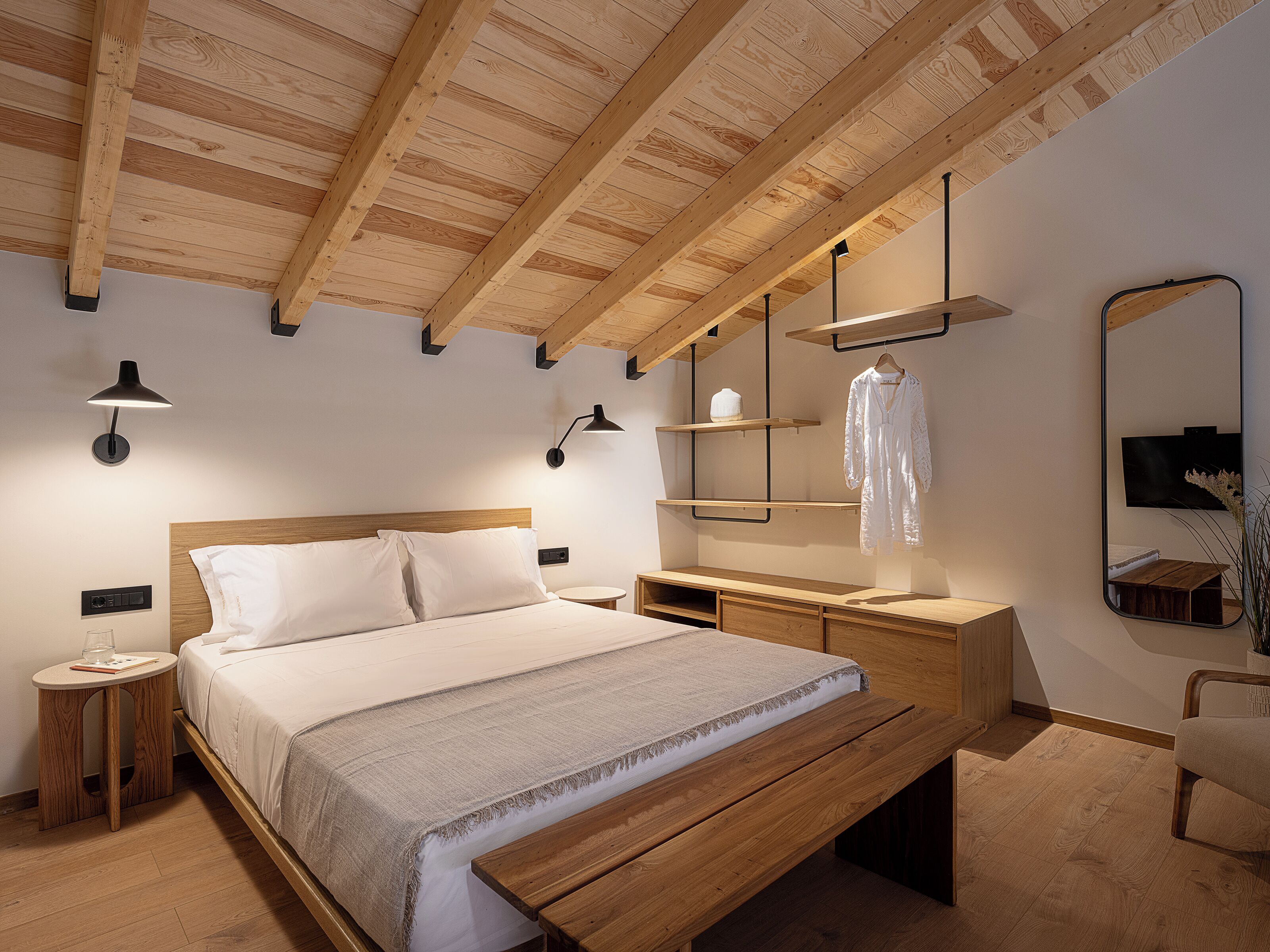 A modern bedroom with a wooden ceiling, a large bed, bedside tables, a mirror, and built-in shelves.
